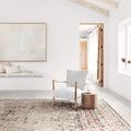 Theia Taupe / Brick Rug displayed in a bright room with vaulted ceiling and wooden beams, styled with a chair and side table.