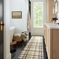 Rug as a runner in a bathroom with black tile floor, wooden cabinets, and natural light