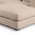 Close-up of the chaise cushion showing soft beige woven fabric texture and low wooden feet