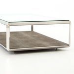 Detail of clear glass edge resting on polished steel framing above brown textured base