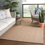 Tan Iver rug styled on outdoor deck between wicker chairs with patterned cushions and greenery