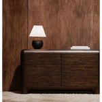 Tuve table lamp on dark wood dresser against matching wood-paneled wall