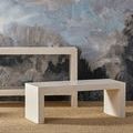 Bench shown at front angle with textured dark blue and gray wall background and woven rug floor