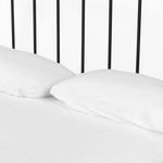 Close-up detail of two white pillows resting against slender vertical bars of black iron bed headboard