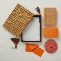 Open box filled with stationery items arranged on a white surface with books and red patterned pouch nearby