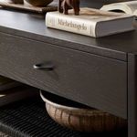 Close-up of decorative books and items on Zuma Coffee Table with textured drawer front and woven shelf underneath
