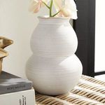 Angled side view of the vase with cream faux orchid, surrounded by stacked books on a rattan surface in sunlight