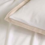 Top view close-up of pillow corner with natural sand satin border on smooth white fabric