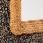 Close-up of bottom right corner showing curved rattan weave and frame texture with floral wallpaper background