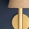 Lindenwood Wall Sconce with aged brass metalwork and grasscloth-covered stem and shade mounted on navy wall
