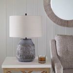 Alternate side view of lamp on side table with glass of amber liquid and textured beige armchair nearby