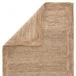Corner of the rug folded over showing woven front and back texture in beige natural fiber