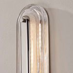 Side view of vertical wall sconce lit with warm light, showing polished silver bar and glass edges