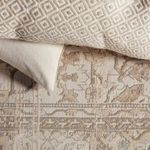 Side angle of rug in room context with neutral colored furniture and decorative pillows.