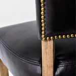Close-up detail of gold nailhead trim along black leather chair back and wood frame