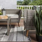 Side view of outdoor seating area showing rug’s trellis pattern and fringed edge beside wicker furniture