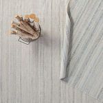 Rug laid out with birch firewood basket on top and corner flipped to reveal blue accents on underside