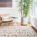 Elka Ivory Multi Rug displayed in a bright room with a wicker chair, side table, and large potted plant