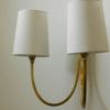 Angled close-up focusing on right sconce’s tapered linen shade and brass arm
