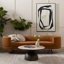Bright room with rust-colored sofa, black and white artwork, and Amaud rug beneath round black pedestal table