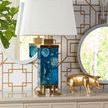 Tobago mirror reflecting decorative table lamp with blue agate base and gold pig figurine on patterned wallpaper