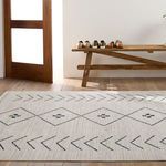 Tribal rug in cream and dark slate near wooden bench with shoes, showing entryway context with natural light