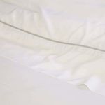Close-up of white bamboo sateen sheet fabric showing subtle sheen and fine stitching detail along edge