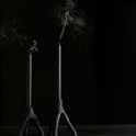 Close-up of two lit tapered candles in black cast iron holders with smoke rising on dark background