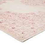Close-up corner view showing rug’s scrolling border and pink floral medallion on white background