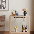 Painting hanging on light wall above rolling bar cart with bottles and wine glasses