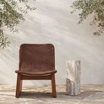 Outdoor setting with table next to brown woven lounge chair on stone patio under natural light