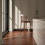 Walnut counter stool in a sunlit modern kitchen corner with marble island and wood flooring