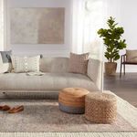 Wide room view framing sofa, woven poufs, and nearby plants on rug