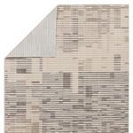 Back corner of rug folded over revealing light gray rug backing with striped pattern