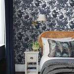 Wallpaper applied on bedroom wall showing bedside table, rattan headboard, and moody styled interior