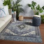 Rug styled on wood floor in an outdoor setting with a sofa, plants, and decor around it.