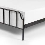 Detailed close-up of bed corner showing solid black iron leg and vertical bars on footboard beneath clean white sheet