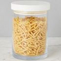 Single clear glass canister with smooth white wood top containing spiral pasta on marble surface