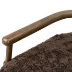 Close-up of smooth oak armrest curve over dark shearling seat texture