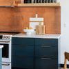 White ceramic pedestal bowl styled with peaches on kitchen counter with copper backsplash and dark blue cabinets