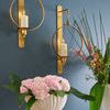 Pair of sconces on blue wall lit with candles above a white planter with pink hydrangeas and tall floral arrangement