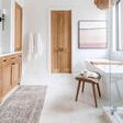 Runner rug in bright bathroom with white marble tile floor and wooden cabinets