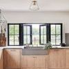 Glint light installed on white ceiling above kitchen sink with black framed open windows and wood cabinets