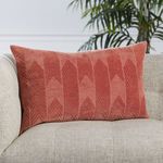 Pink chevron lumbar pillow on beige couch with green leafy plant in soft focus background