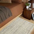 Partial view of Tallulah Mist Ivory Rug beside bed with brown bedding and wooden nightstand