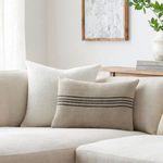 Pillow on neutral sectional sofa with other cushions, framed wall art and wooden console table in background