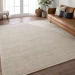 Taupe rug installed in a living room with leather couch, decorative pillow, and plant