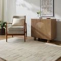 Max Sandstone Handmade Rug shown in a bright living room with mid-century armchair and wood cabinet