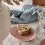 Close-up of mauve rose oval plate holding a piece of seeded bread with linen napkin and glass nearby