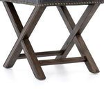 Front profile of ottoman focusing on crossed wood legs and leather cushion with brass nail accents